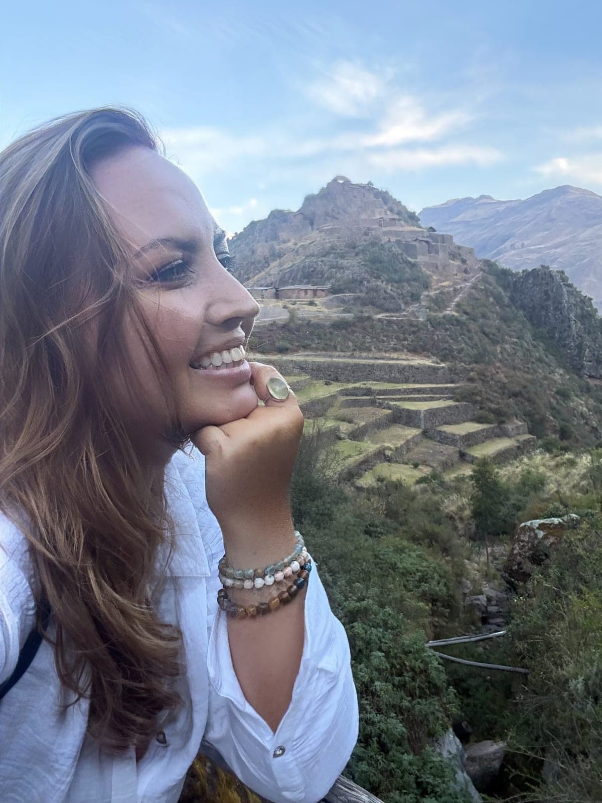 Sarah smiling, chin resting on her hand, with hillside Inca terraces and ruins behind her