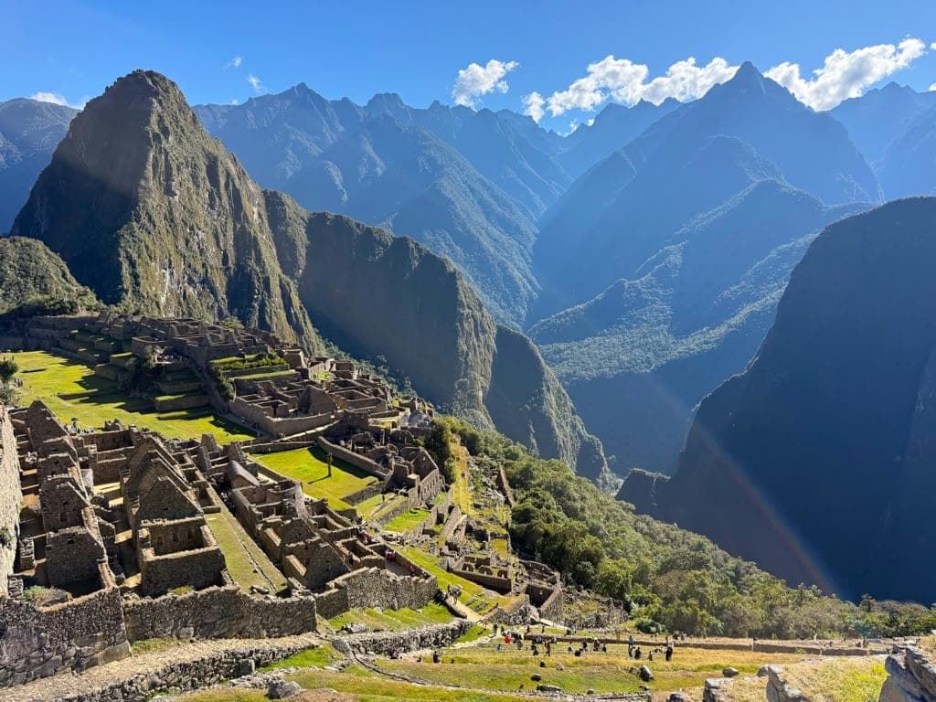 The stone terraces and buildings of Machu Picchu spread below its peak, with green valleys and the ridge line of the Andes beyond