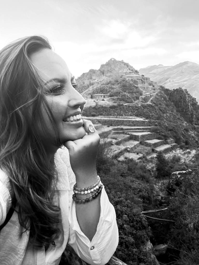 Sarah resting her chin on her hand, smiling, with Andean terraces and mountains behind her