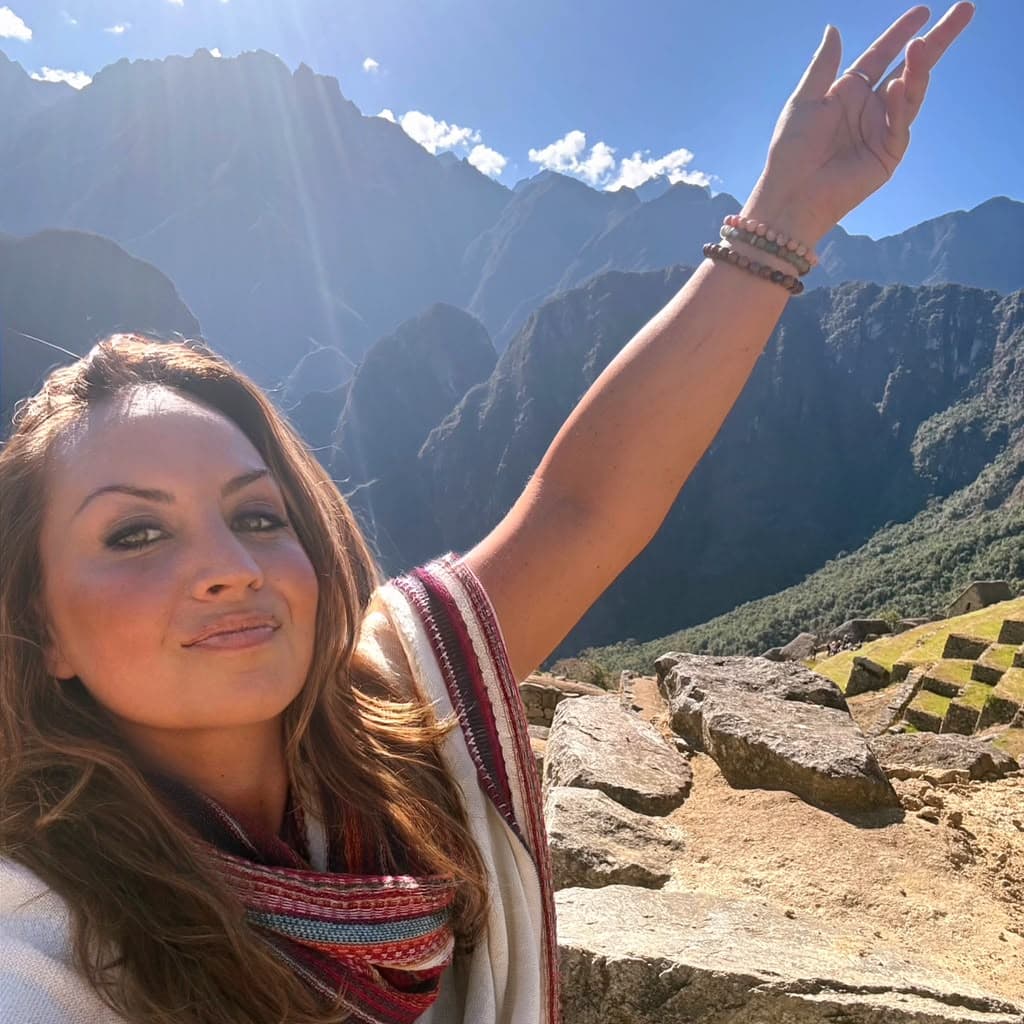 Sarah reaching toward the peaks above Machu Picchu in the morning sun, a woven scarf around her shoulders