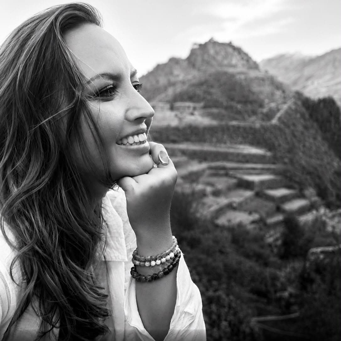 Sarah in profile, chin resting on her hand, smiling out over a terraced hillside, in black and white